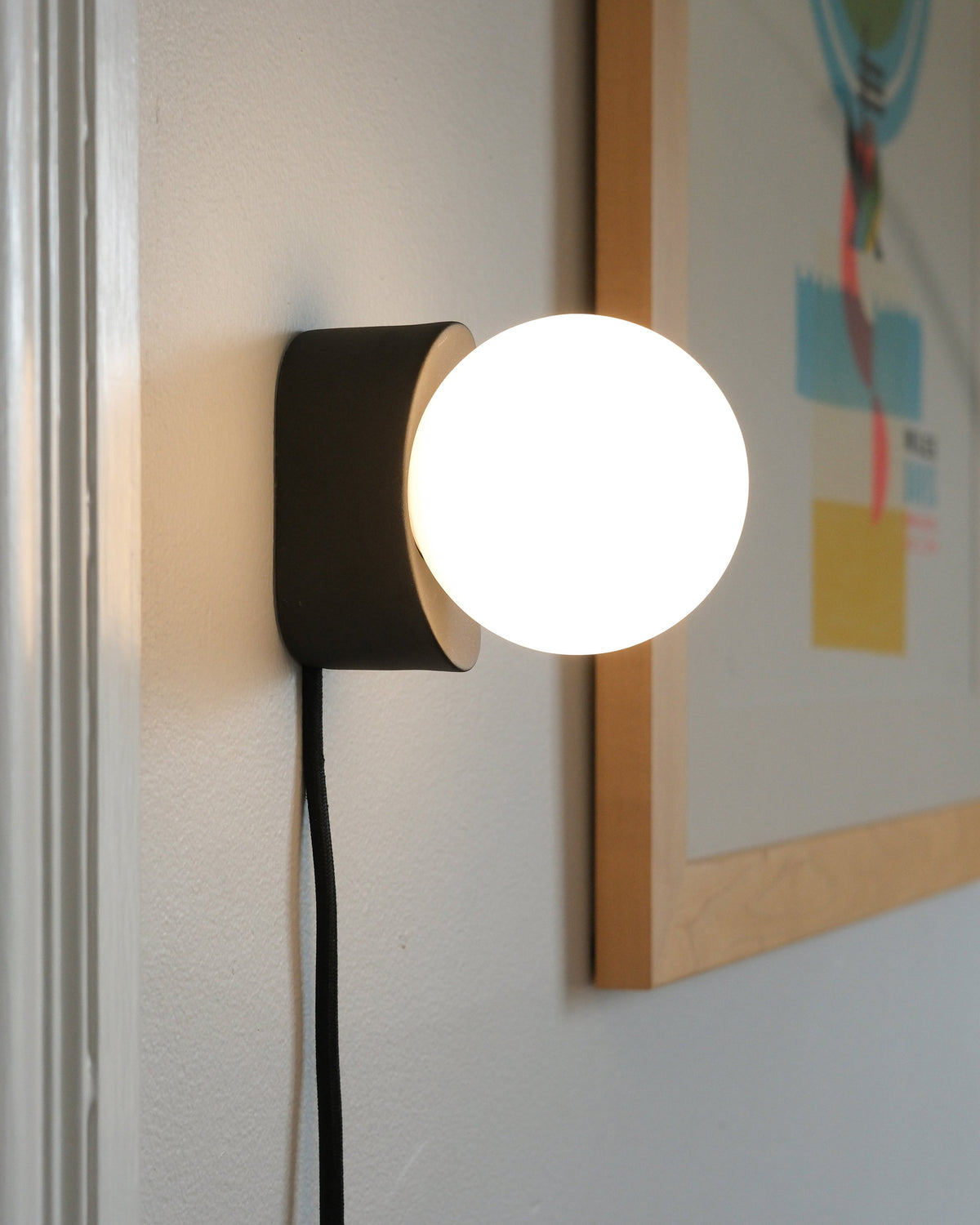 Iota Sconce in Black, lit, close view