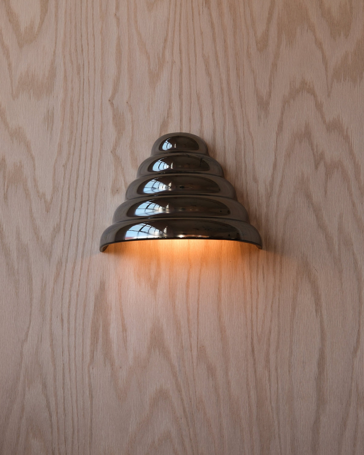 Ripple Conical Sconce in Chrome, lit, on a wood wall