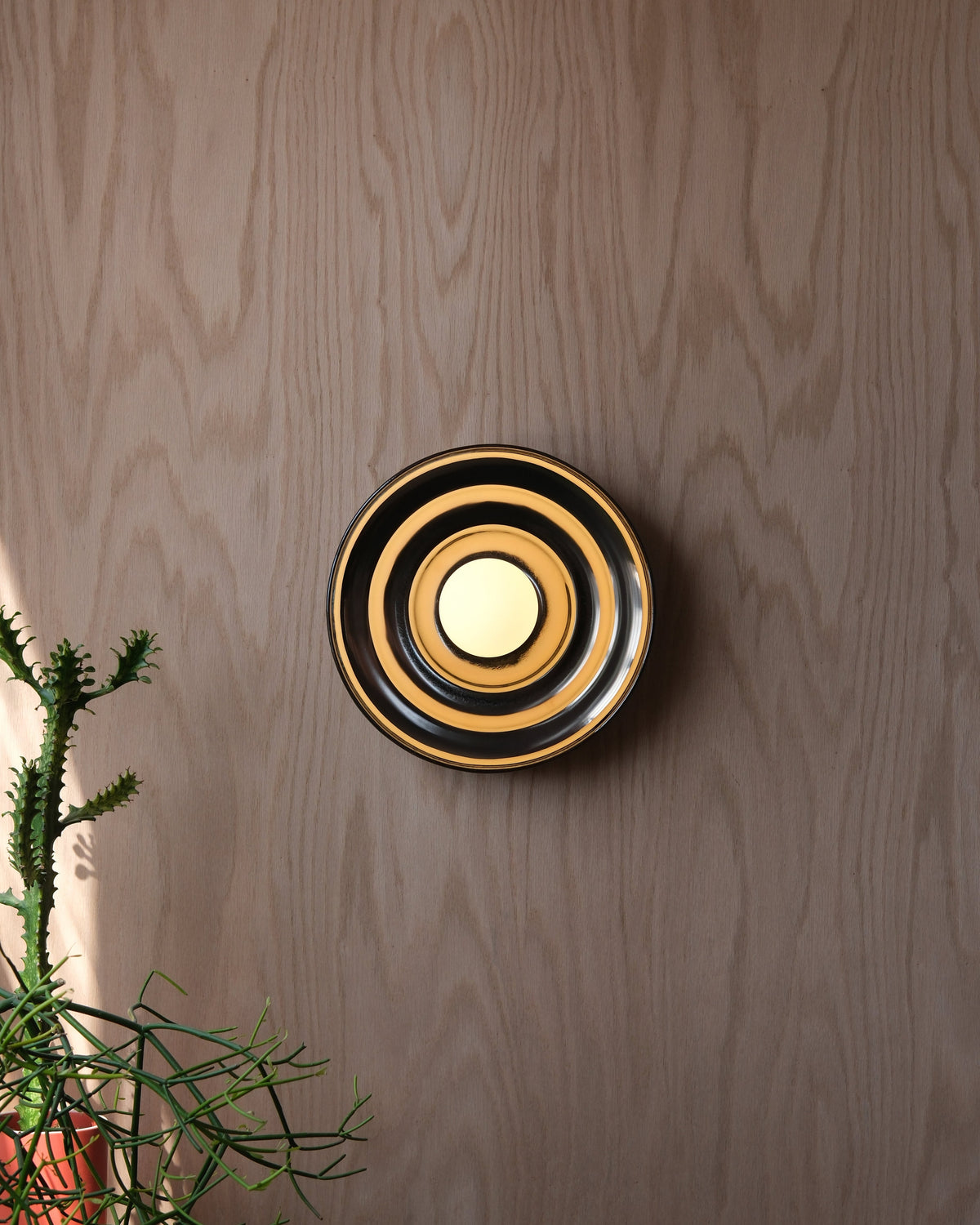 Ripple Bowl Sconce in Chrome, lit, on a wood wall