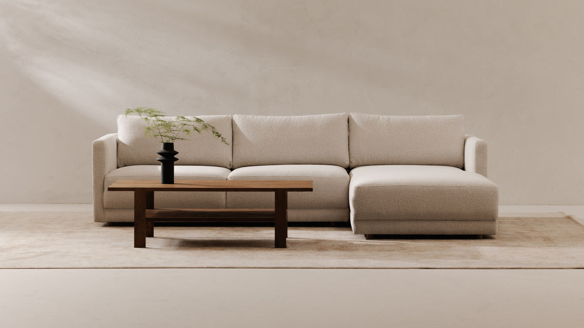 Moe's Home Collection Bryn sectional in oyster, a nubby cream upholstery, with a right-facing chaise, photographed against a plaster wall with a low walnut coffee table and a black vase of asparagus fern in front of it