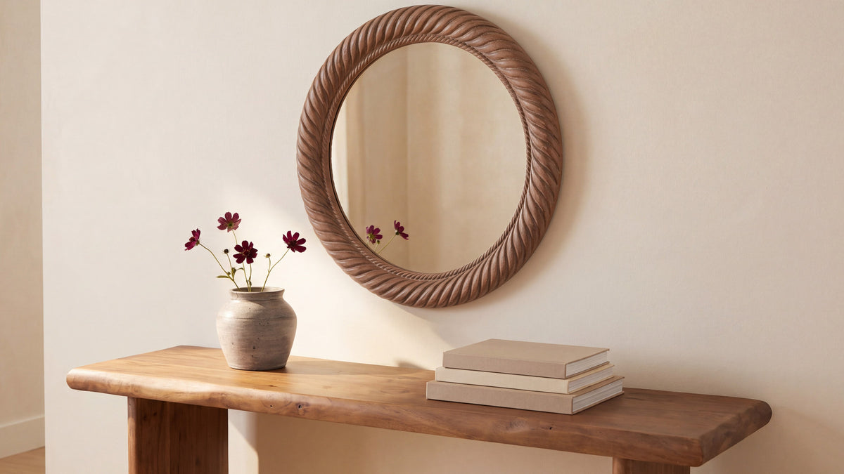 The small Delphine mirror on a plaster wall above a live-edge console, a ceramic vase of red cosmos below it and books stacked to one side