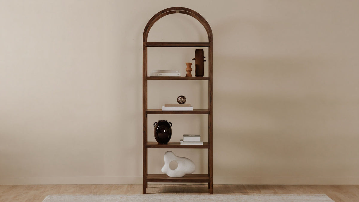 Moe's Home Collection Eero bookcase in walnut, an arched frame of four shelves with books and ceramics, against a plaster wall