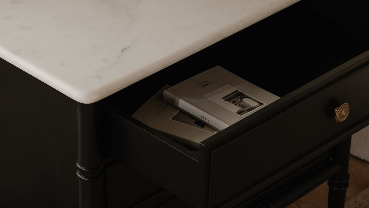 A drawer of the Moe's Home Collection Eleanor nightstand pulled open to show two books inside, the antique brass ring pull and turned black leg catching the light below the white marble top