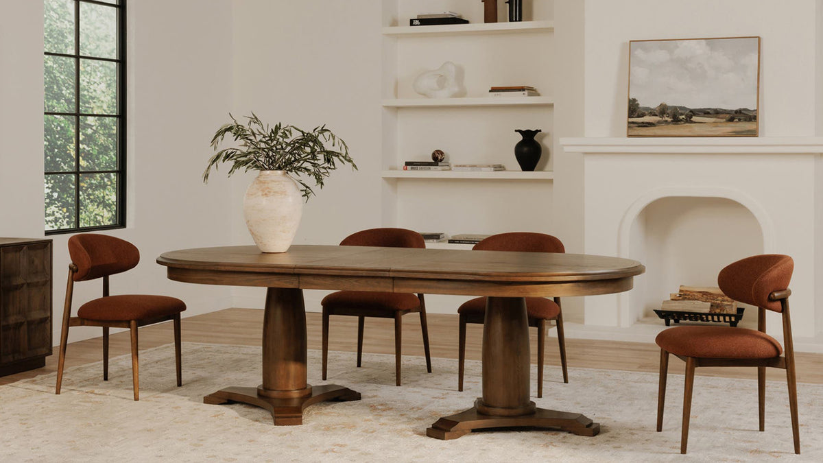 Five Moe's Home Collection Ellie dining chairs in rust around an oval pedestal dining table in a bright room with a plaster fireplace, built-in shelves and a landscape painting
