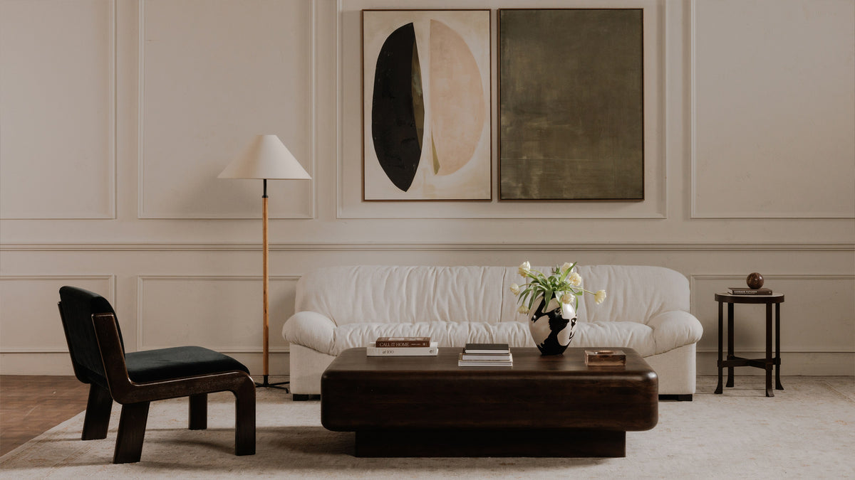 Moe's Home Collection Eton coffee table in dark brown acacia, centred on a pale rug in a panelled living room with a cream boucle sofa, a dark wood and black upholstered lounge chair, a conical floor lamp, two large abstract canvases and a slim black side table, styled with art books, a black and white vase of white tulips and a copper tray