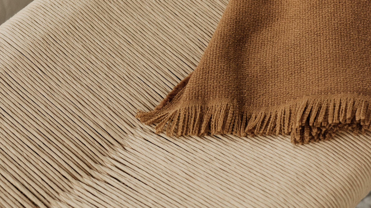 Close overhead view of the Hawthorn bench's woven natural-fibre rope seat, with a fringed rust throw laid across it