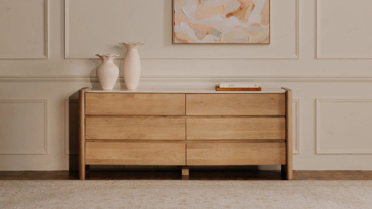 Moe's Home Collection Lane oak dresser with its Botticino marble top in a bedroom, six drawers below the rounded overhang