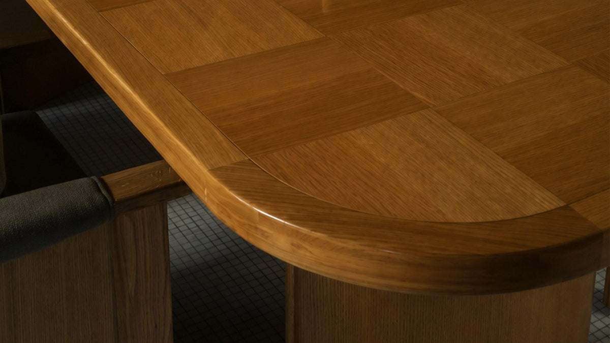 Close view of the Mallory dining table's domed end, showing the solid oak edge band running around the curve and the oak parquet squares meeting it at a fine scribe line