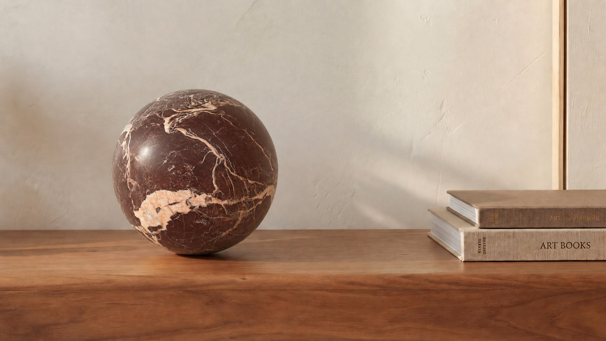 The Odessa sphere in red levanto marble on a walnut surface beside art books, deep red stone crossed by cream veining