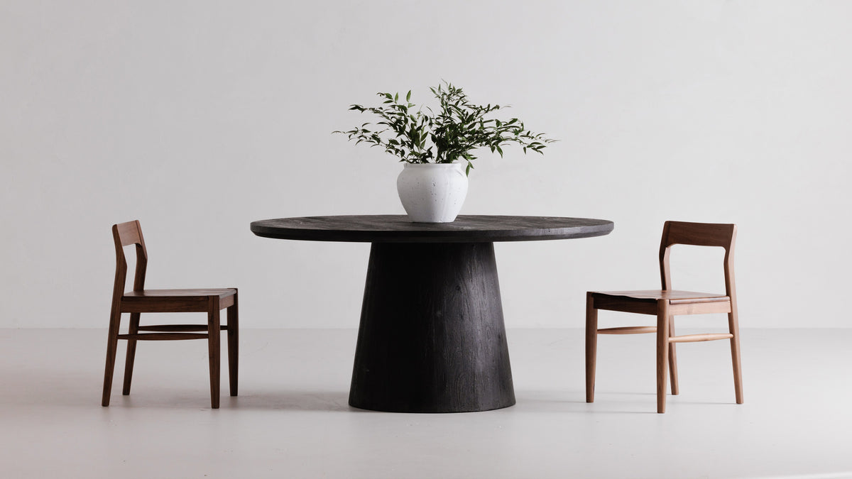 Two Moe's Home Collection Owing dining chairs facing each other across a black round pedestal table, one in walnut brown and one in natural oak, against a white studio wall