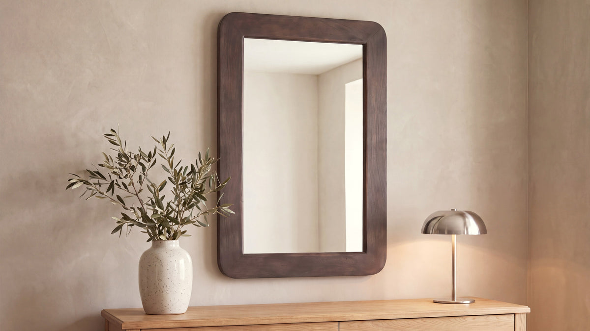The rectangular Perth mirror above a pale wood sideboard, its rounded acacia frame in warm brown, beside a stone vase of olive branches and a small domed lamp