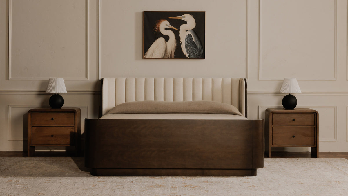 A pair of Moe's Home Collection Riley nightstands in oak flanking a dark walnut bed with a channel-tufted cream headboard, each carrying a round black lamp, beneath a framed painting of two herons
