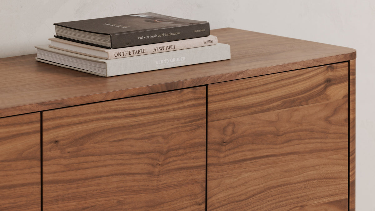Close view of the Moe's Home Collection Round Off sideboard in walnut brown, showing the rounded corner, the door seams and a stack of books on the top