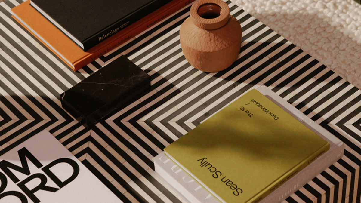 Overhead close view of the Terning coffee table's black and white striped bone veneer top, with the chevron pattern running beneath stacked art books, a black stone box and a terracotta vase