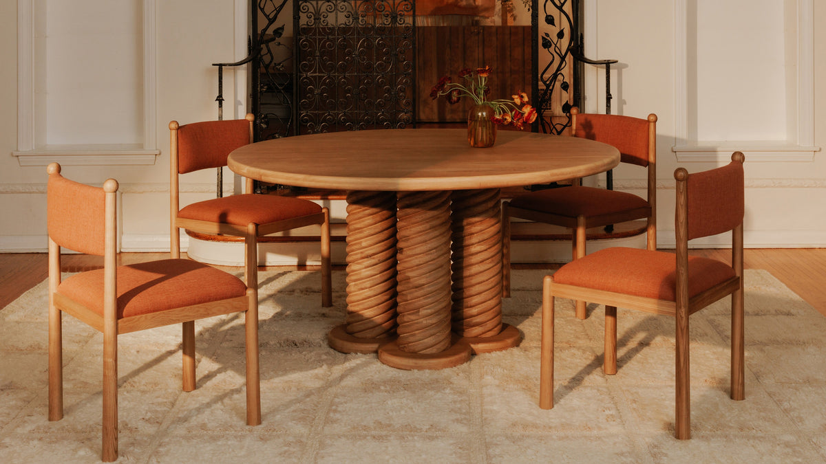 Four Moe's Home Collection Villetta dining chairs in deep pink around a round oak table with a carved twisted base, in a panelled room with an antique iron fire screen behind