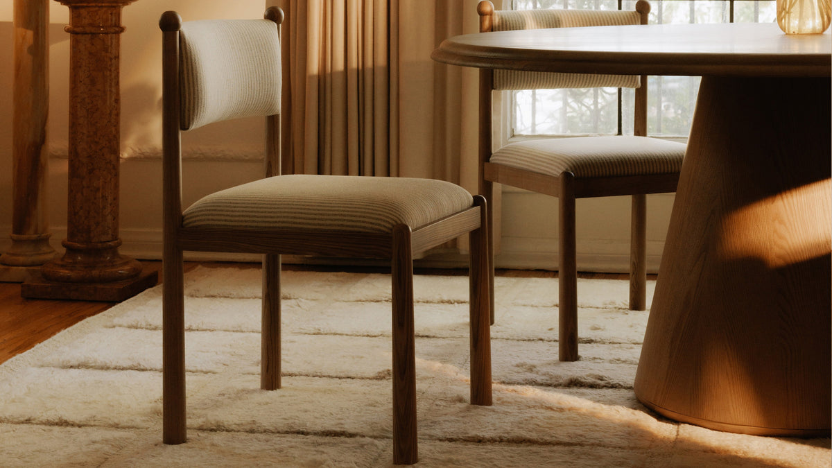 A close view of two Moe's Home Collection Villetta dining chairs in gray stripe in low afternoon light, showing the turned finial at the top of each rear post and the padded high back