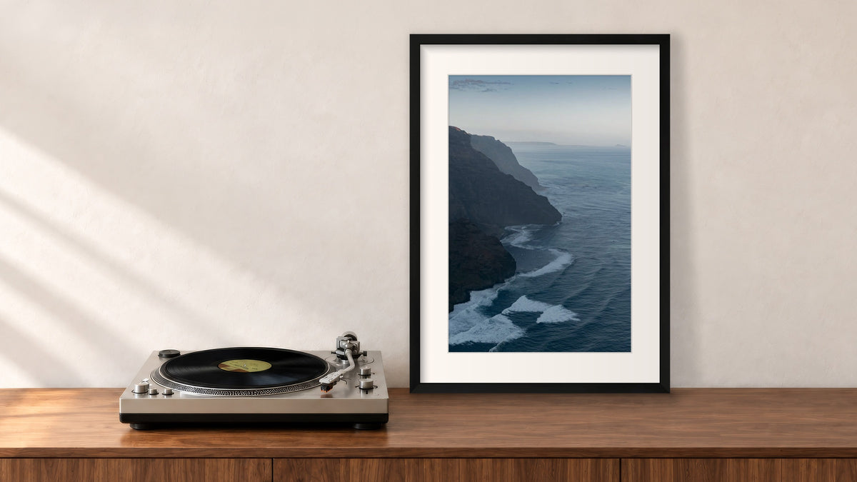 Nāpali Coast Framed Photograph in a black frame, leaning on a walnut console beside a turntable