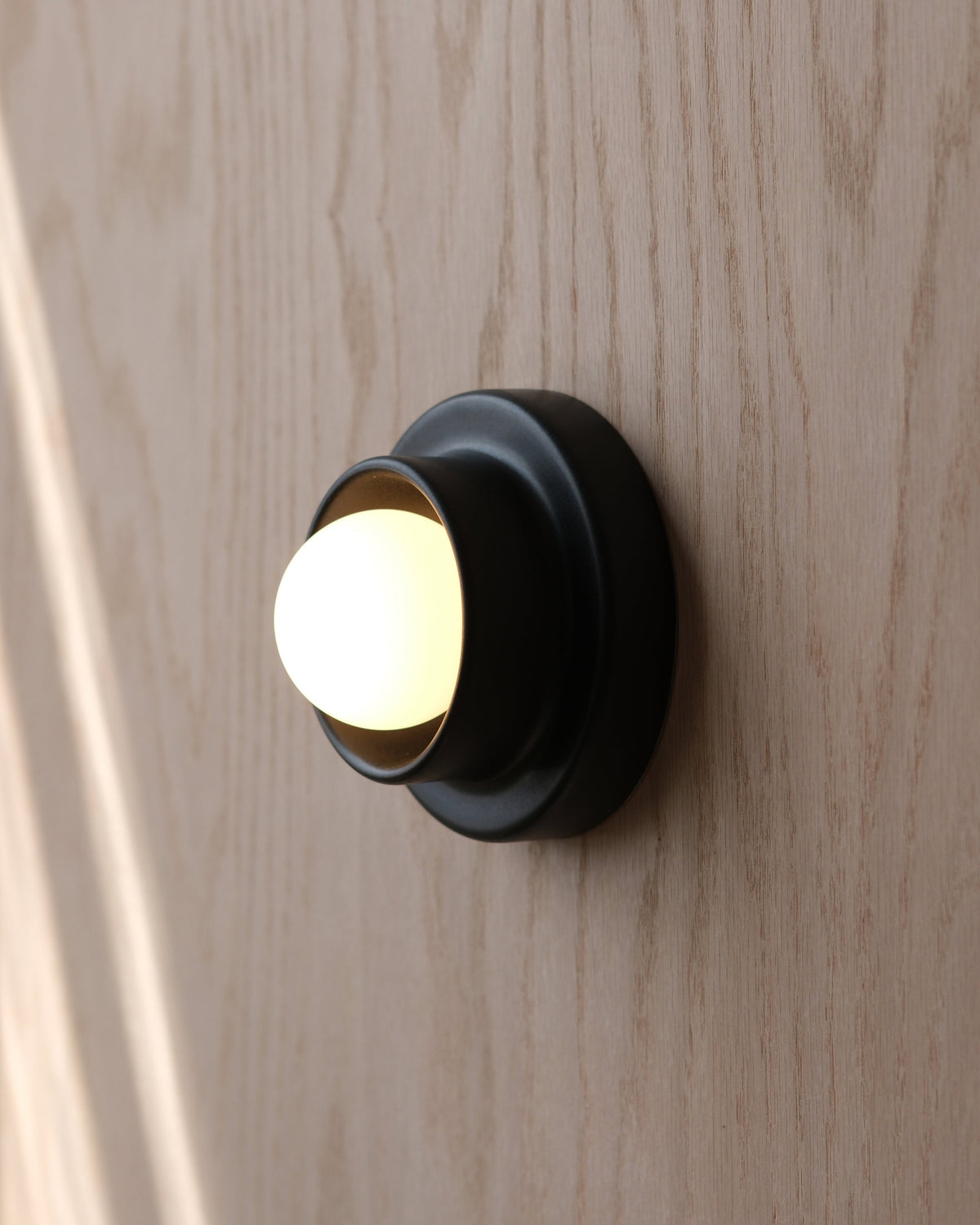 Q Sconce in Black on a wood wall
