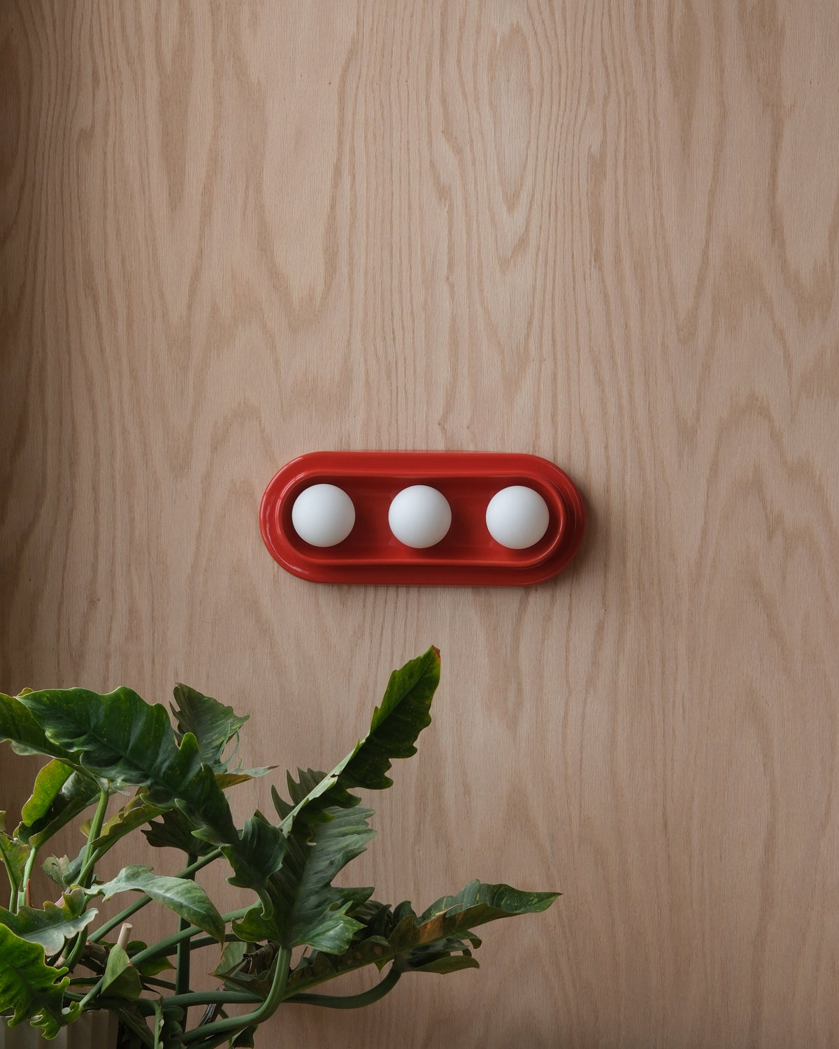 Q Triple Sconce in Red, mounted horizontally on a wood wall