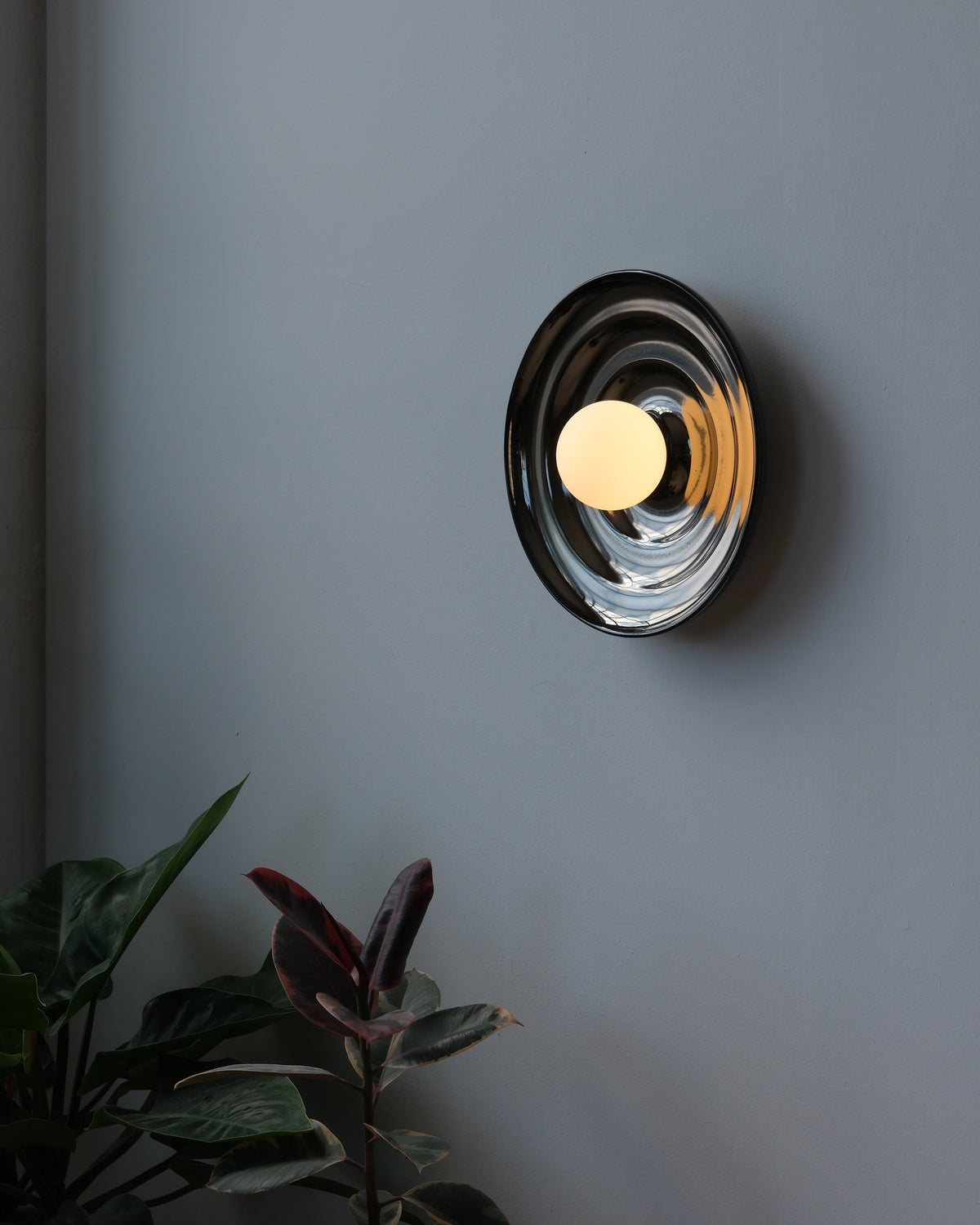 Ripple Bowl Sconce in Chrome, lit, on a dark wall