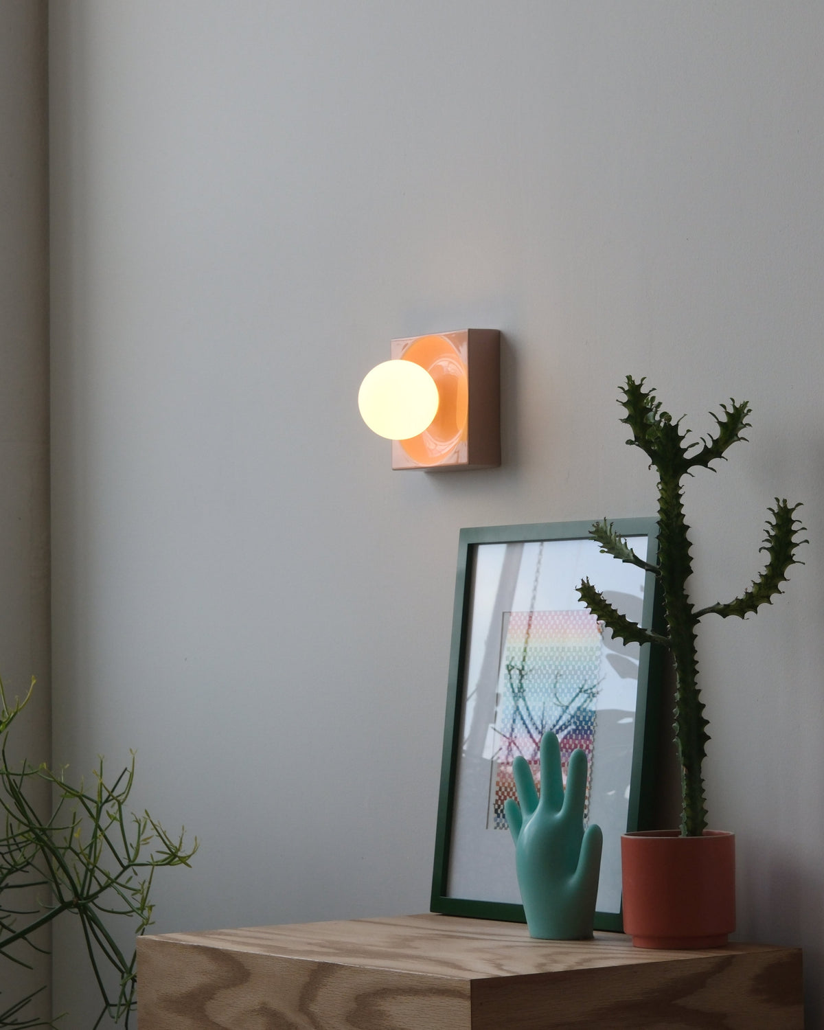 Cubic Sconce in Pink Glossy above a plywood cabinet