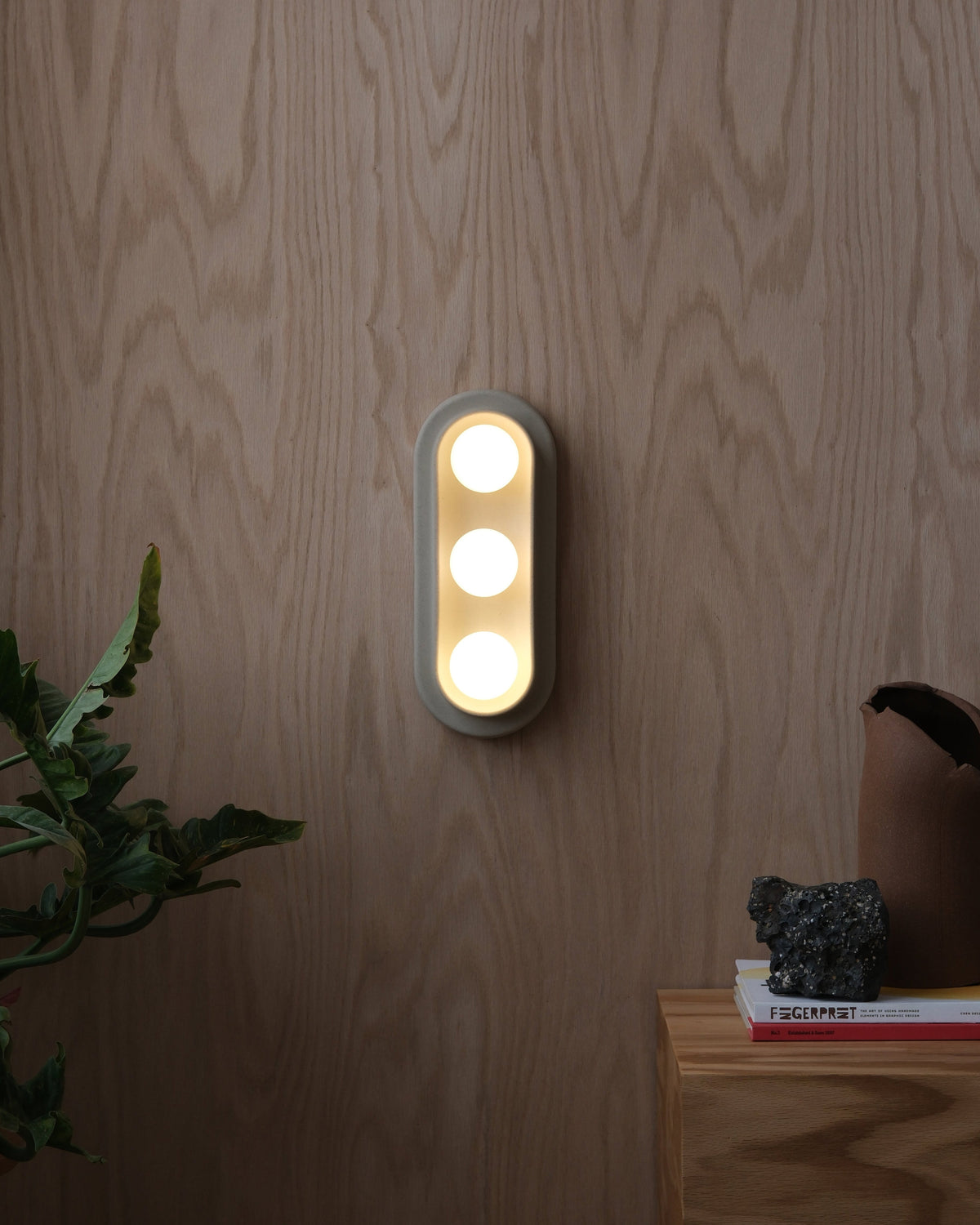Q Triple Sconce, lit, on a wood wall