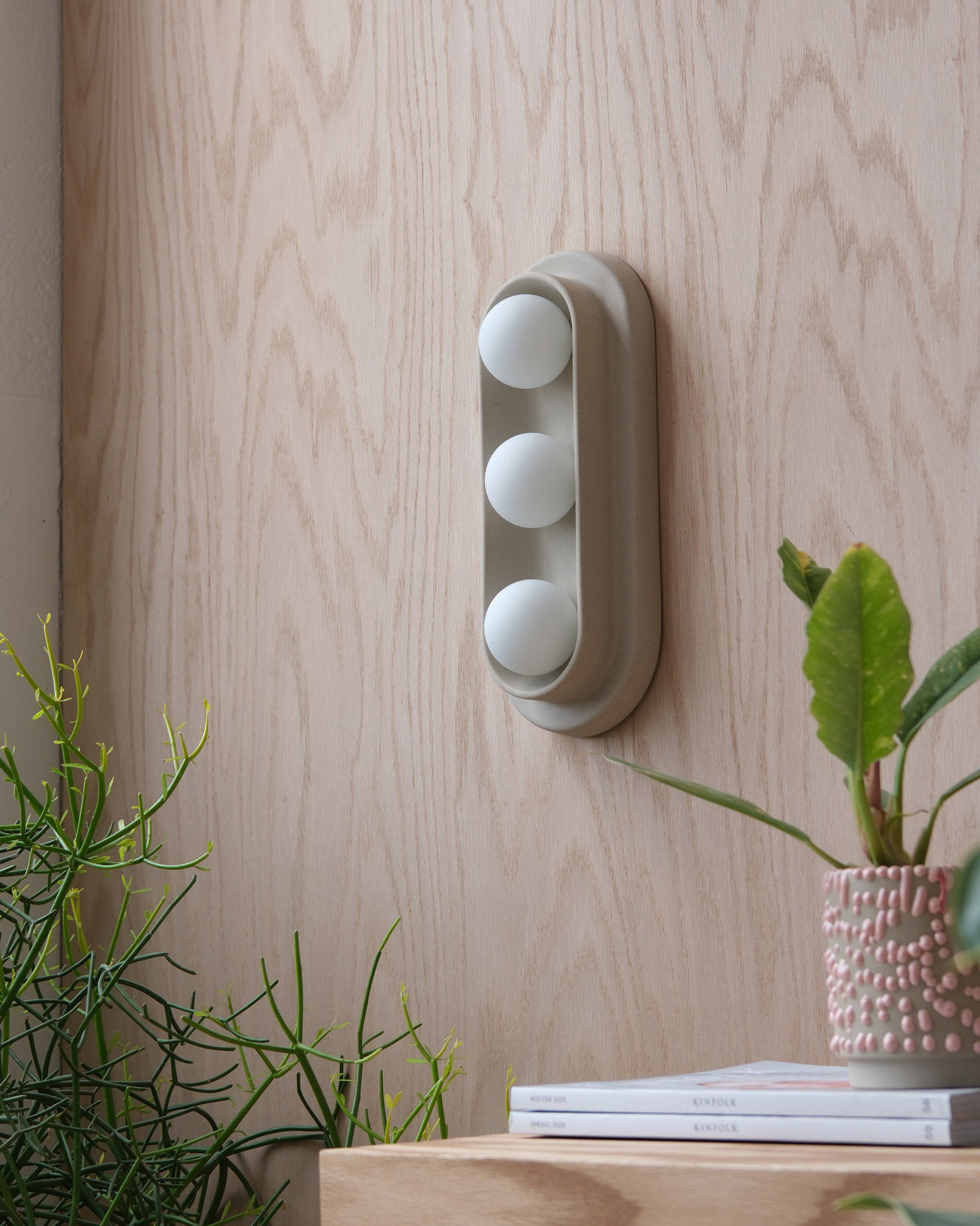 Q Triple Sconce in Dune on a wood wall