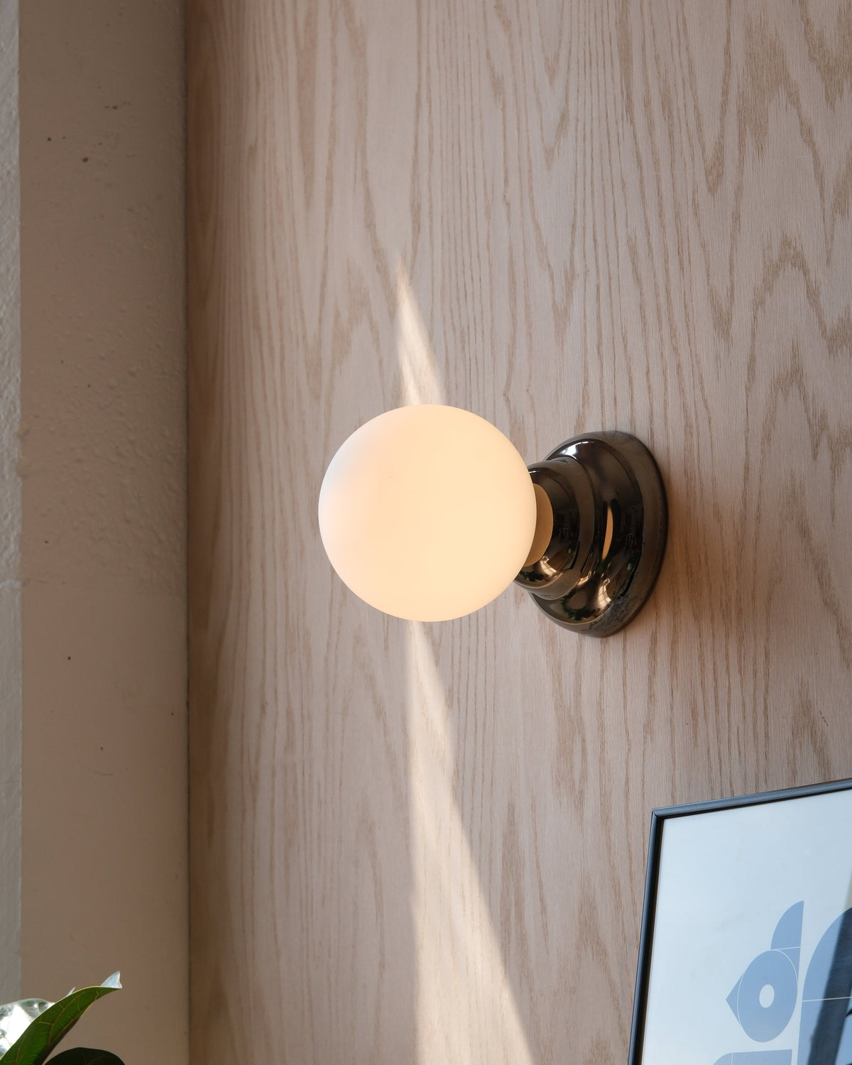 Ripple II Sconce in Chrome, lit, on a wood wall