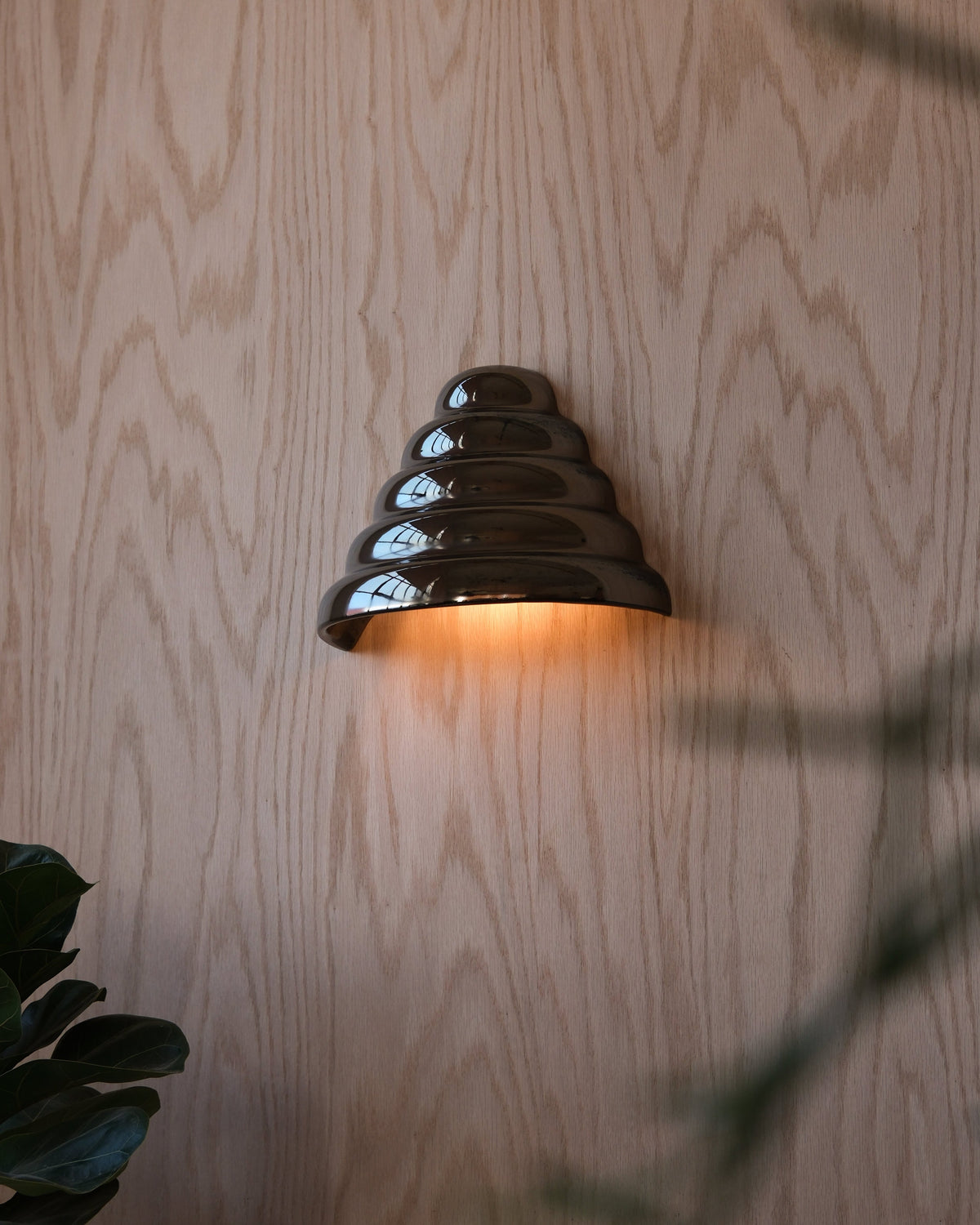 Ripple Conical Sconce in Chrome, lit, on a wood wall