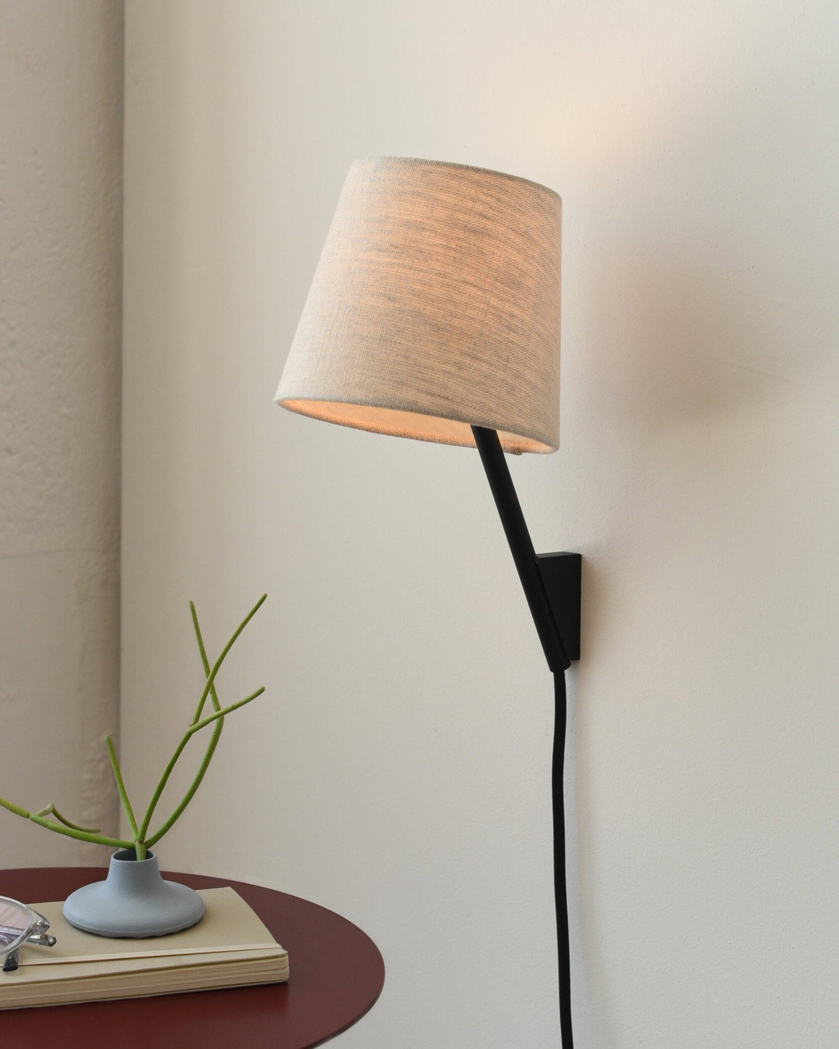 Tokyo Sconce in Black, lit, beside a side table