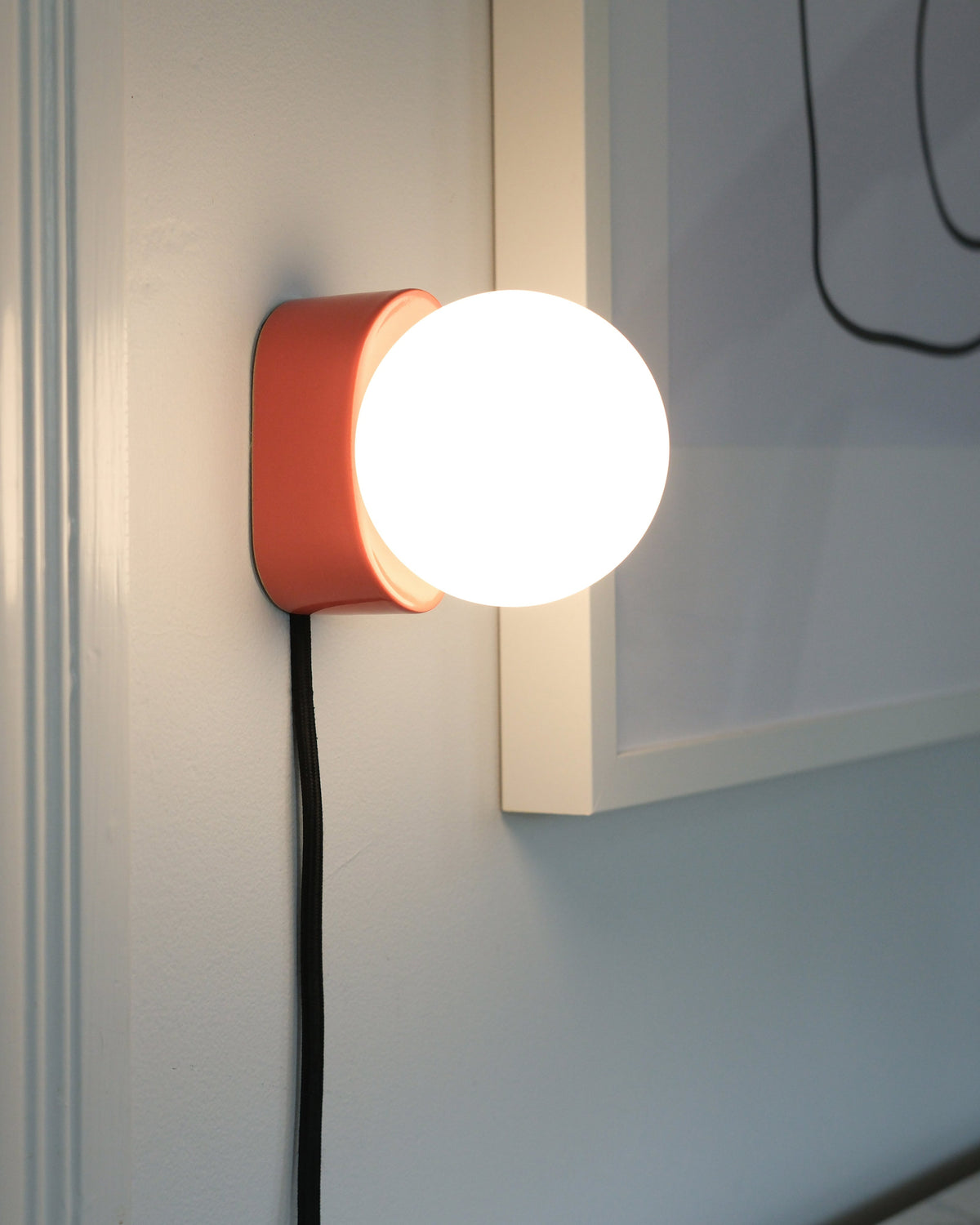 Iota Sconce in Vermilion, lit, beside framed art