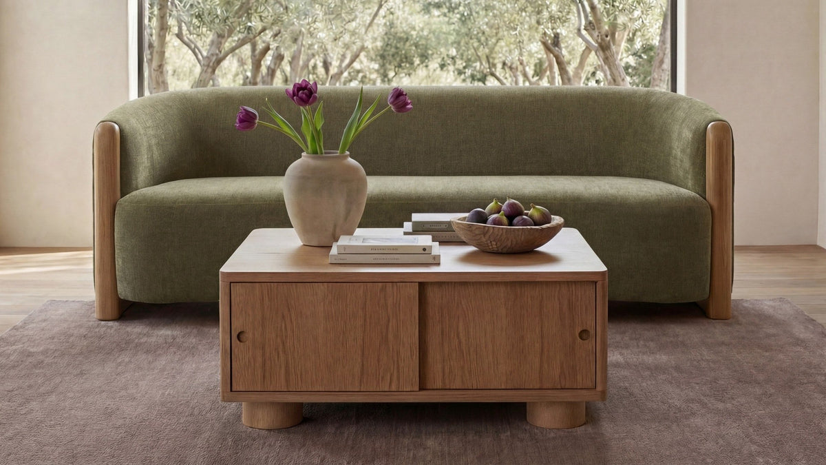 Moe's Home Collection Anya sofa in olive chenille, its curved back and rounded oak corner posts seen straight on in a bright room, with an olive grove through a full-height window behind it and a low oak coffee table in front