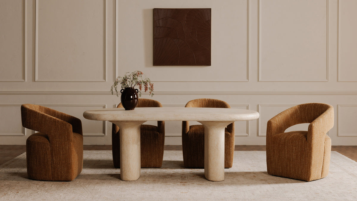 Four Moe's Home Collection Barrow rolling dining chairs in amber glow around an oval travertine dining table in a panelled room, showing the curved barrel backs from behind and in profile
