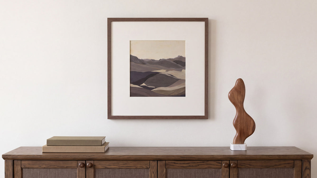 The Caledonia framed painting above a dark oak sideboard, its layered desert landscape matted in white inside a brown pine frame, beside a curved walnut sculpture