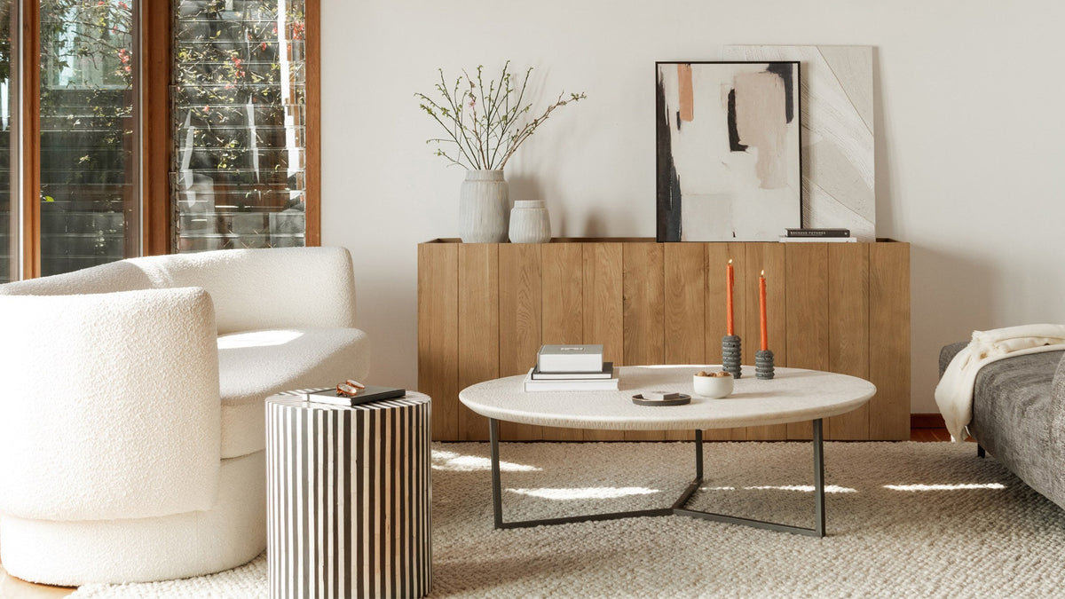 Moe's Home Collection Chameau side table in black and white camel bone, its striped cylindrical form beside a cream boucle swivel chair in a sunlit living room with an oak sideboard and a round stone coffee table