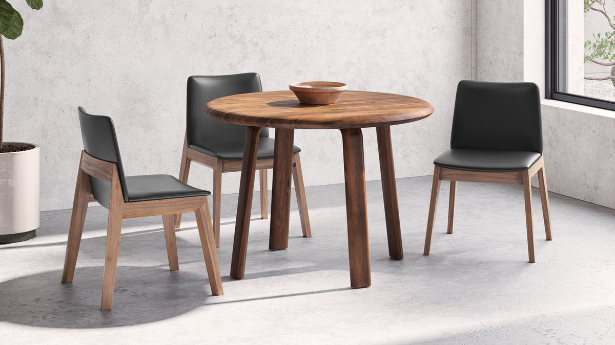 Three Moe's Home Collection Deco dining chairs in ebony vegan leather on solid walnut frames around a round walnut table, on a polished concrete floor beside a window