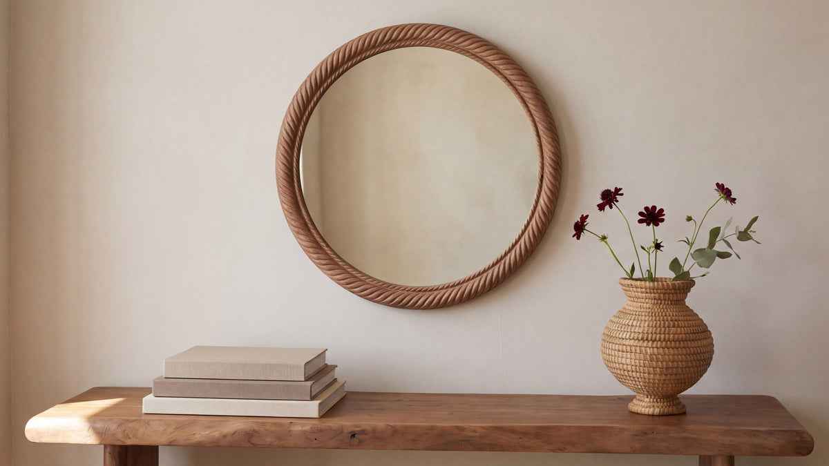 The large Delphine mirror hung above a live-edge wooden console, its rope-twist frame in natural mango, beside a woven vase of dark red cosmos and a stack of pale books