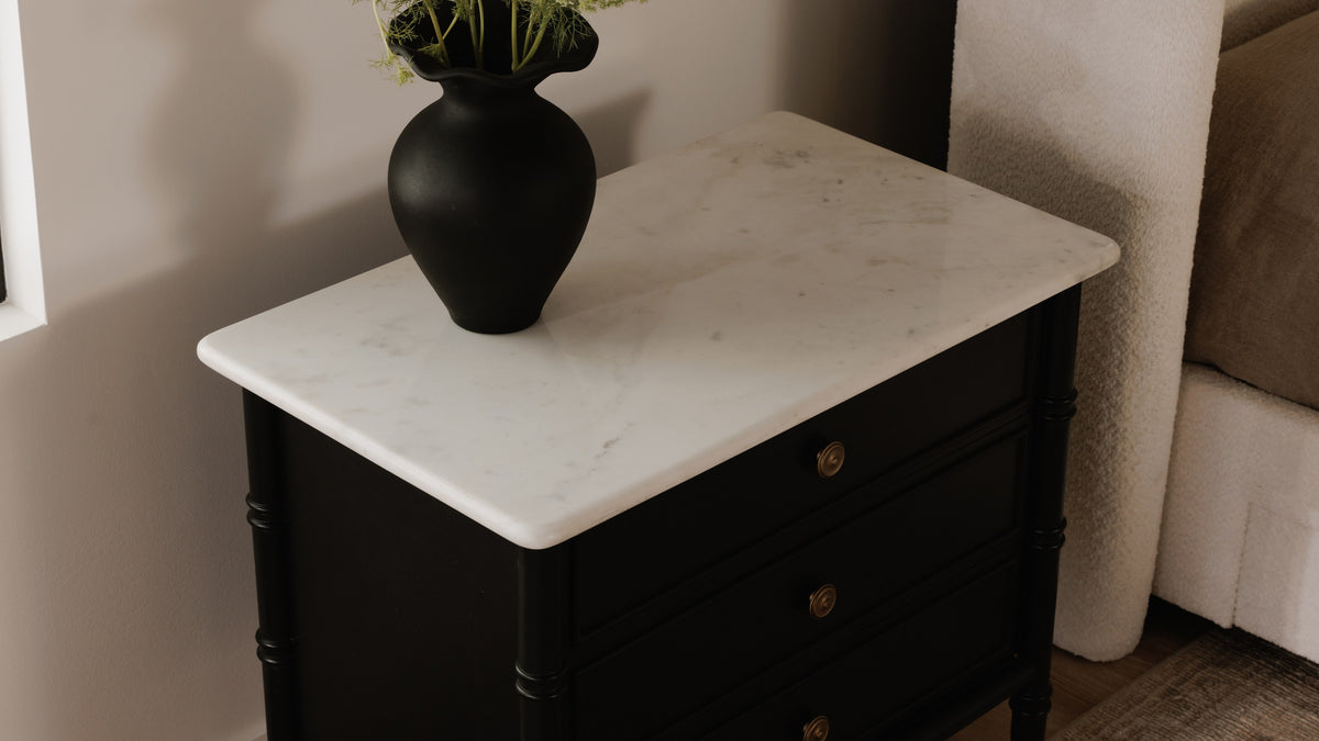 Close view of the Moe's Home Collection Eleanor nightstand's white Banswara marble top, its grey veining running across the polished surface above the matte black case and reeded corner posts