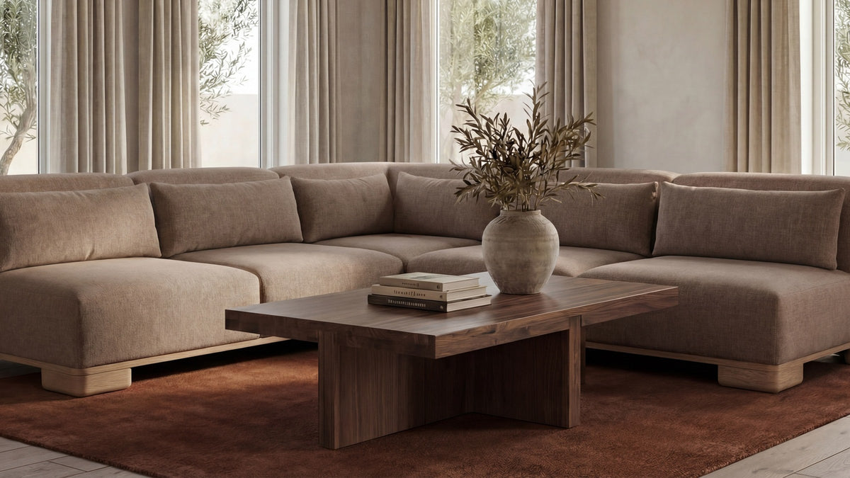 Moe's Home Collection Folke rectangular coffee table in solid walnut, its thick slab top and T-shaped base on a rust wool rug beside a taupe sectional in a curtained room
