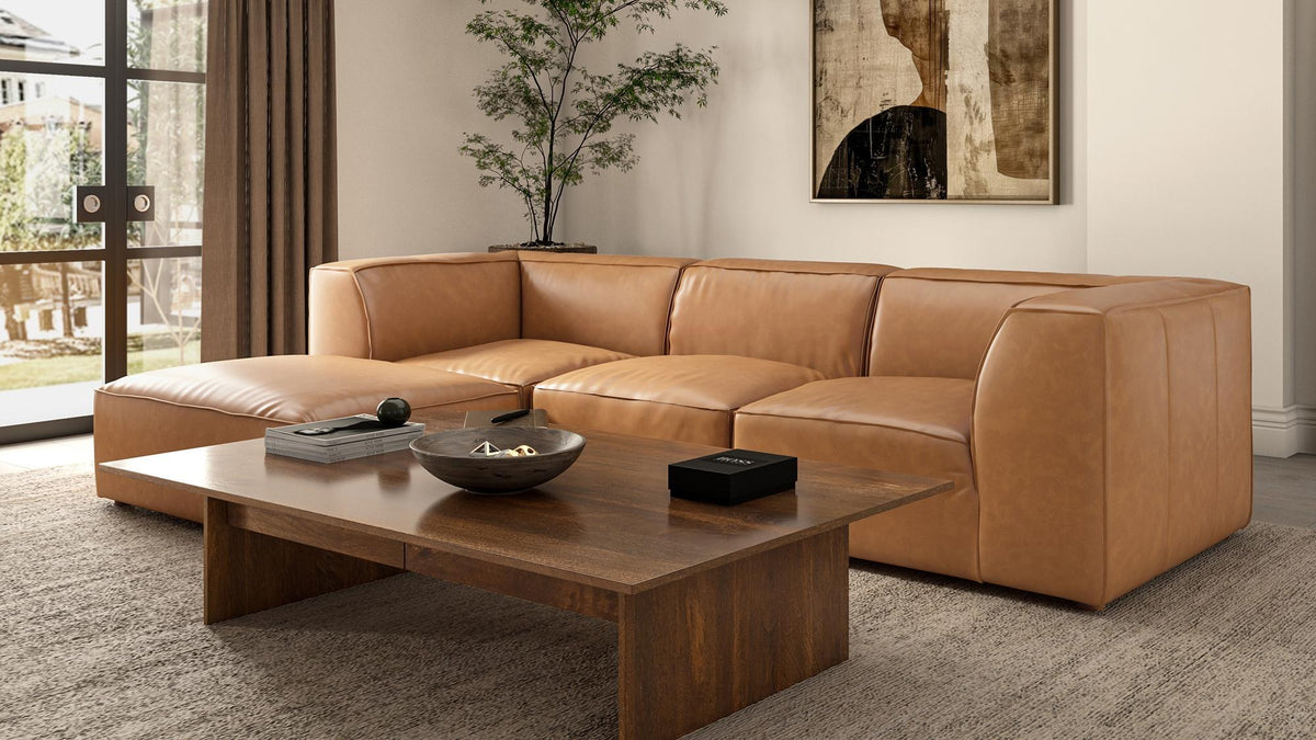 Form ottoman in Sonoran tan top-grain leather beside a low walnut coffee table, its plump rounded form sitting flush against the seating