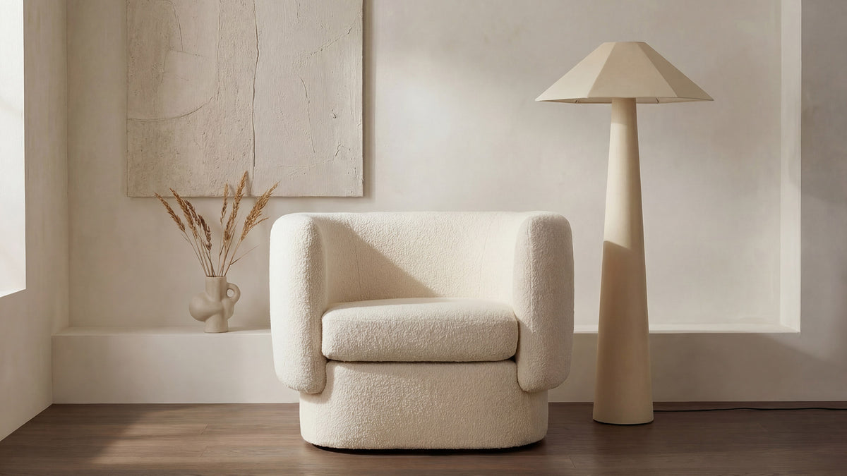 Moe's Home Collection Gigi floor lamp in cream, its fabric-wrapped conical base and wide geometric shade standing beside a cream boucle swivel chair against a plaster wall, with dried grasses in a sculptural vase and a pale abstract canvas above