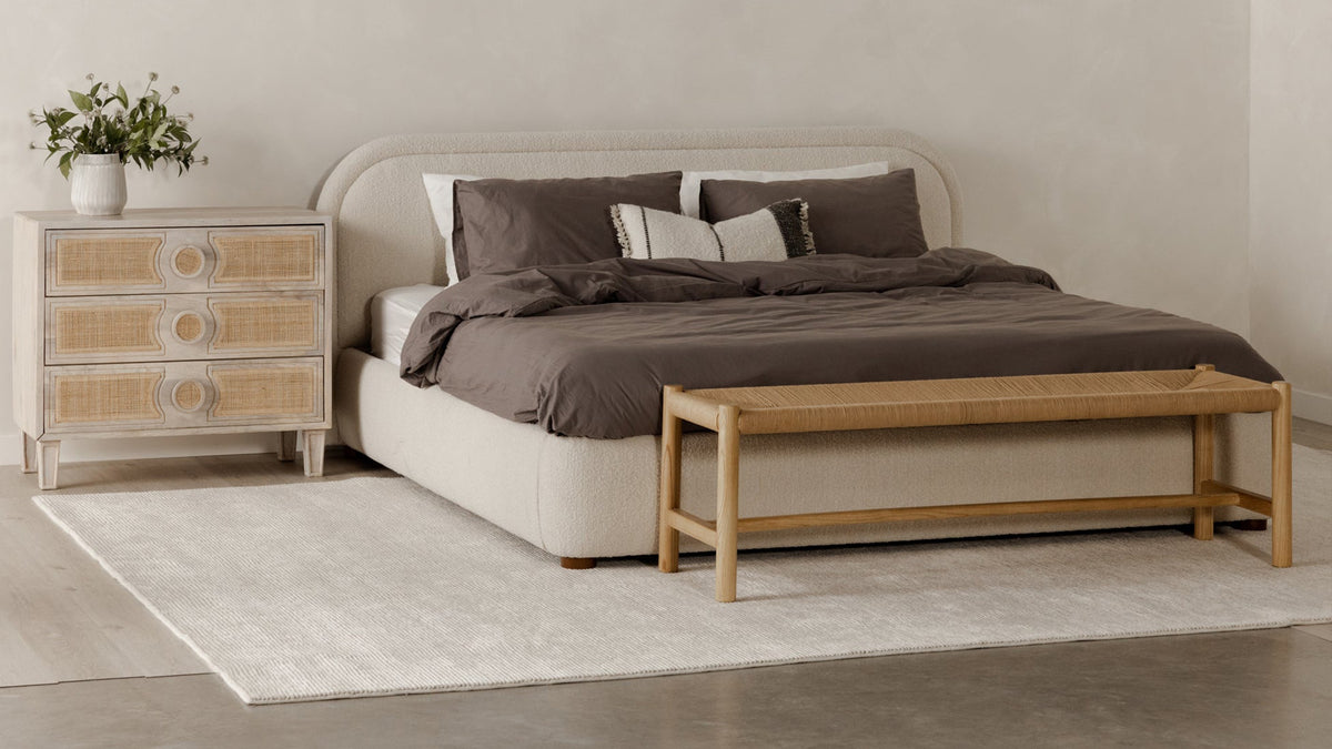 Moe's Home Collection Hawthorn bench in natural elm with a woven rope seat, at the foot of an upholstered bed beside a caned chest of drawers