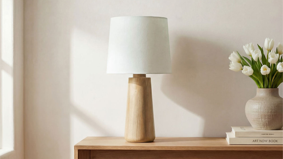 The Ivy table lamp on a wooden console, its tapered solid mango base and pale fabric shade beside white tulips in a ribbed ceramic vase