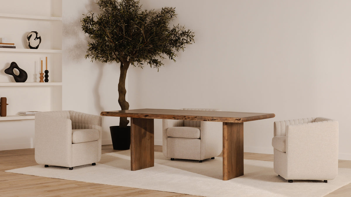Moe's Home Collection Lila dining table in brown acacia on a cream rug, its live edge showing dark natural voids along the length, with three pale upholstered swivel chairs, a potted olive tree and open shelving behind