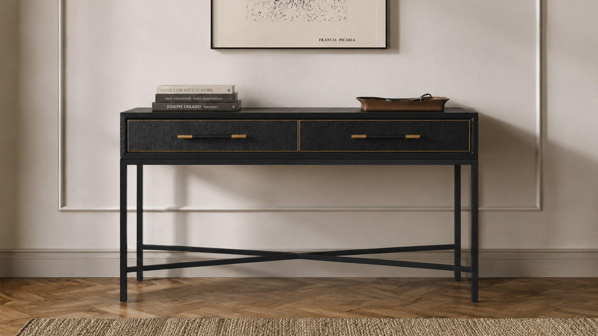 Moe's Home Collection Mako console table in black, styled with stacked books and a shallow dish below a framed print, on a herringbone wood floor