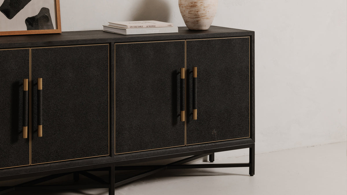Angled view of the Moe's Home Collection Mako sideboard in black, showing the brass trim framing each door panel and the X-braced black metal base beneath