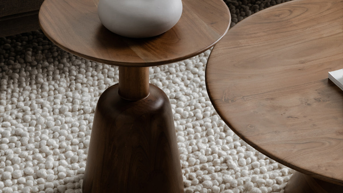 Moe's Home Collection Nels end table in dark brown acacia, its bell-shaped pedestal base and round top seen close on a chunky ivory wool rug, with the matching Nels coffee table alongside