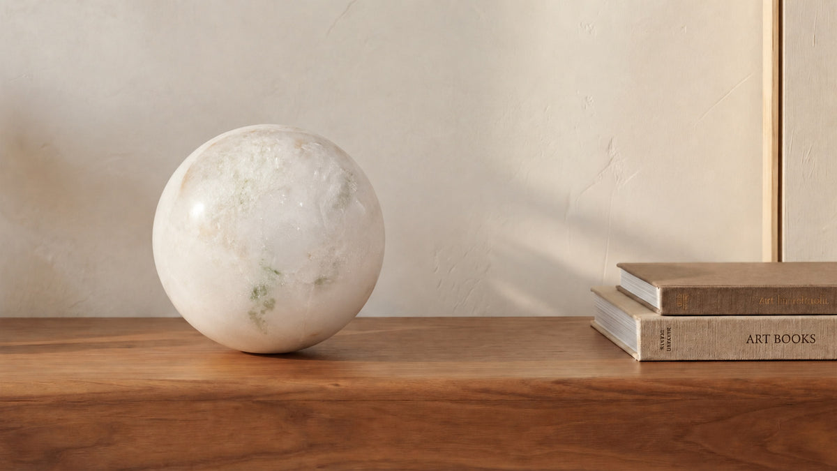 The Odessa sphere in green onyx marble on a walnut surface next to stacked art books, its pale surface faintly clouded with green