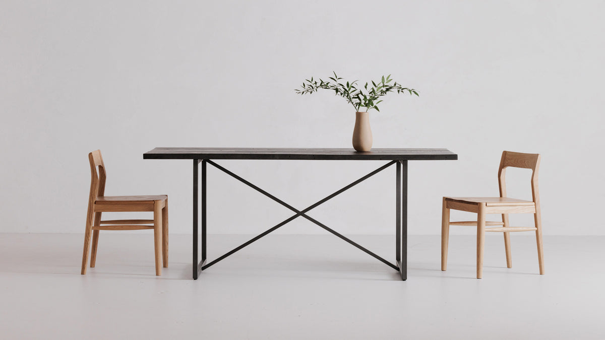 Two Moe's Home Collection Owing dining chairs in natural oak either side of a dark plank table on a cross-braced metal base, in a white studio