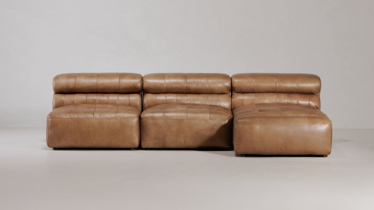 Ramsay modular sectional in tan top-grain leather against a plain wall, two armless slipper chairs beside a chaise, showing the unbroken seat line where the pieces meet